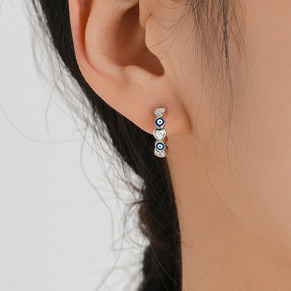 Woman wearing small evil eye hoop earrings with heart-shaped crystals