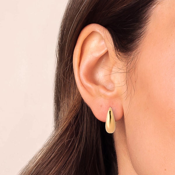 Woman wearing thick gold teardrop huggie hoop earrings