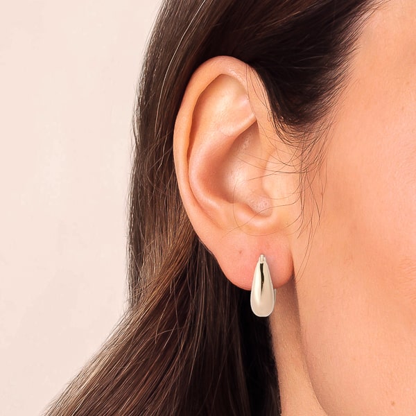 Woman wearing thick silver teardrop huggie hoop earrings