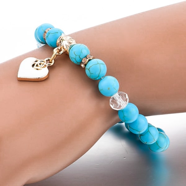 Woman wearing a beaded turquoise stone bracelet with a gold heart charm