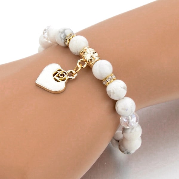 Woman wearing a beaded white marble bracelet with a gold heart charm