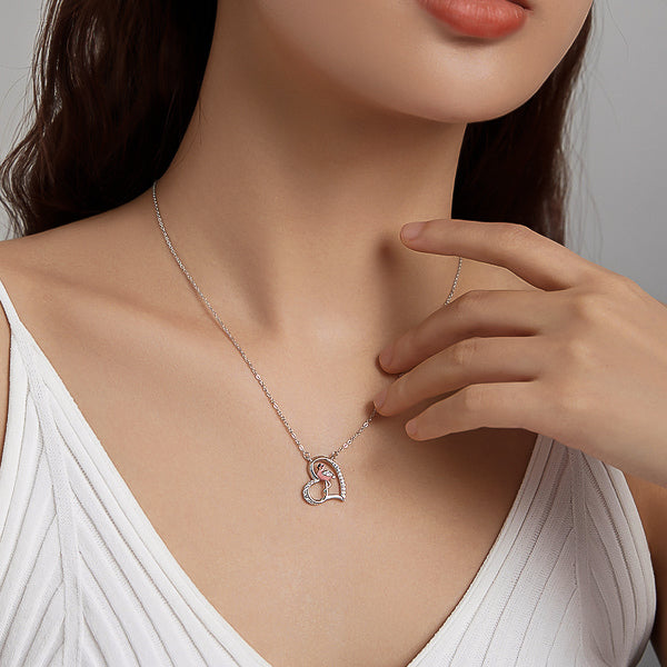 Woman wearing a silver necklace with a heart and a pink flamingo pendant
